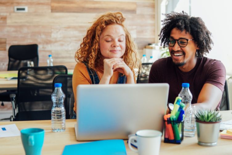 A young woman and a young man smile while looking at a laptop