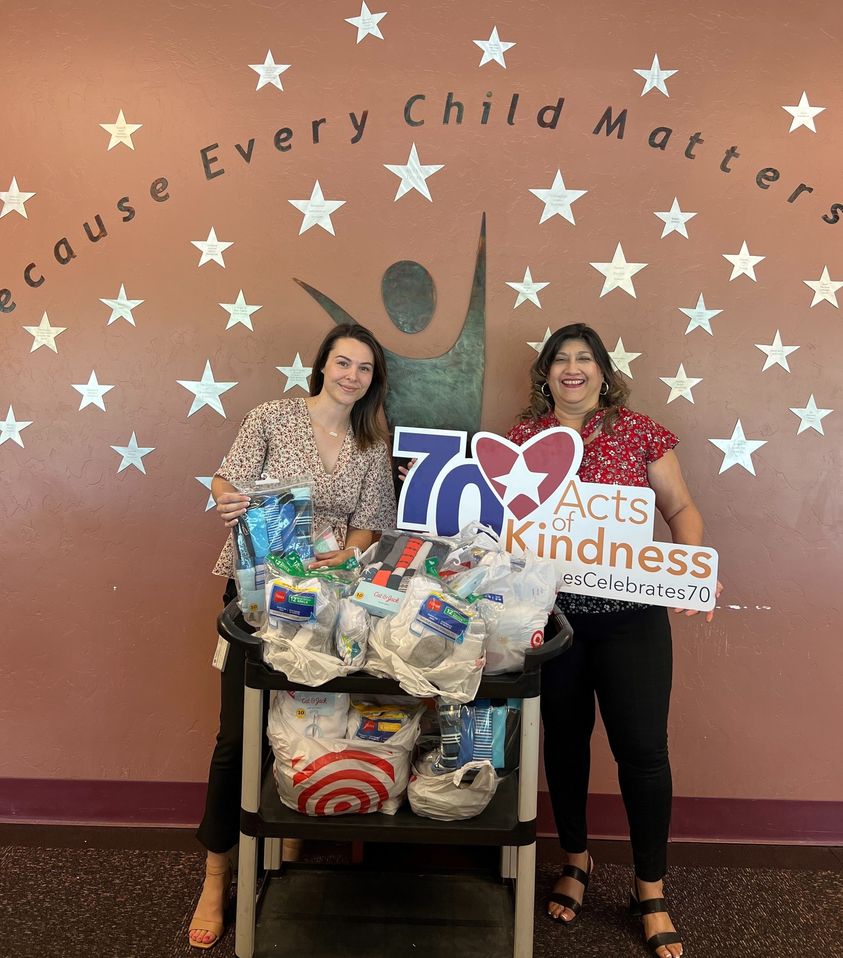Hughes employees stand with 70 Acts of Kindness sign in front of supplies