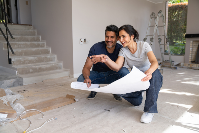A happy couple remodeling their home with blueprints in hand.