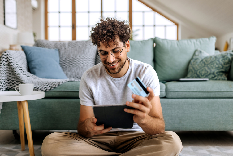 A young man holds his tablet with a credit card in hand, ready to make a purchase online.