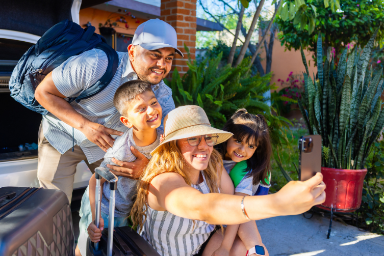 A Latino family poses for a photo with their suitcases and their car.