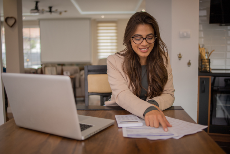 A young woman does her taxes, with papers and a laptop on the table.