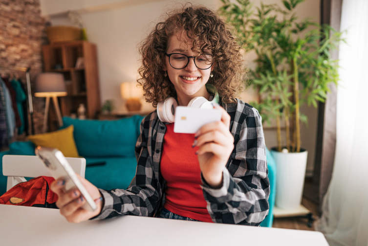 A teenage girl holds a debit card with her phone in the other.