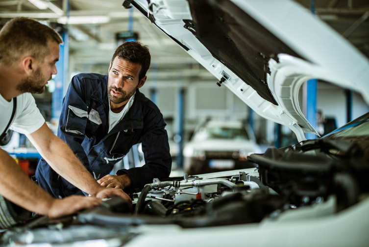 Two auto mechanics talking while working on car engine in a workshop