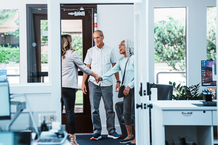 A woman shakes the hand of another older women. A man stand alongside them in a financial institution.