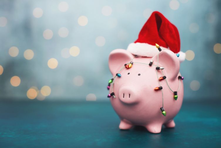 A pink piggy bank wearing a Santa cap wrapped in Christmas lights.