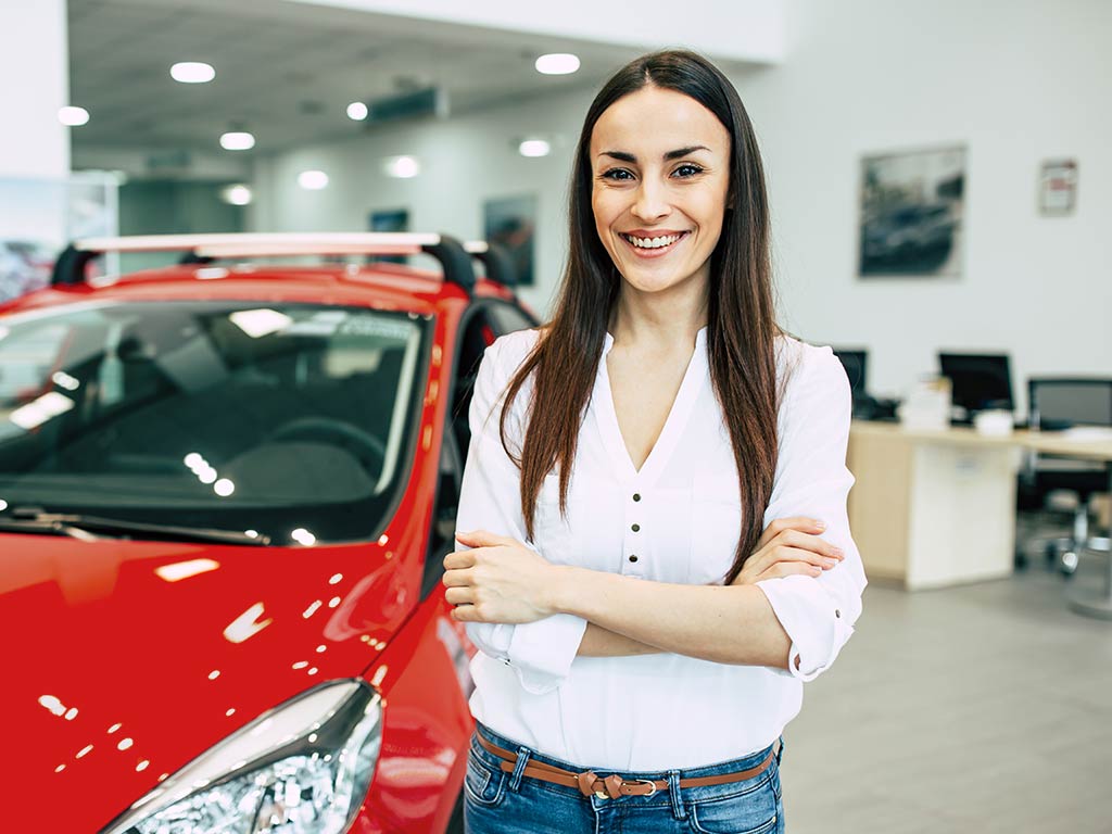 Woman standing in car showroom next to a red car