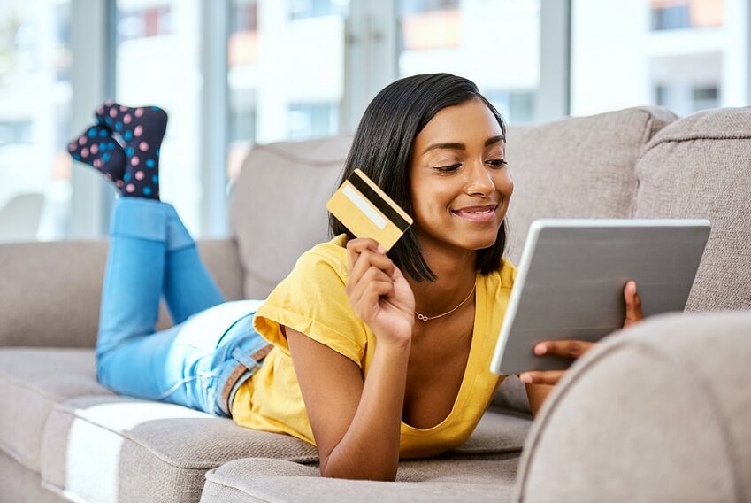 Woman on couch, smiling at iPad, and holding credit card